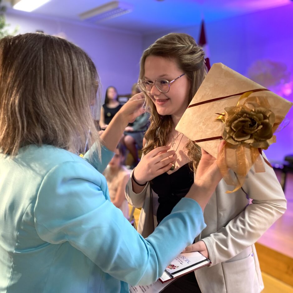 Alise Ozola saņem skolas žetonu no skolotājas Sandijas Joņinas